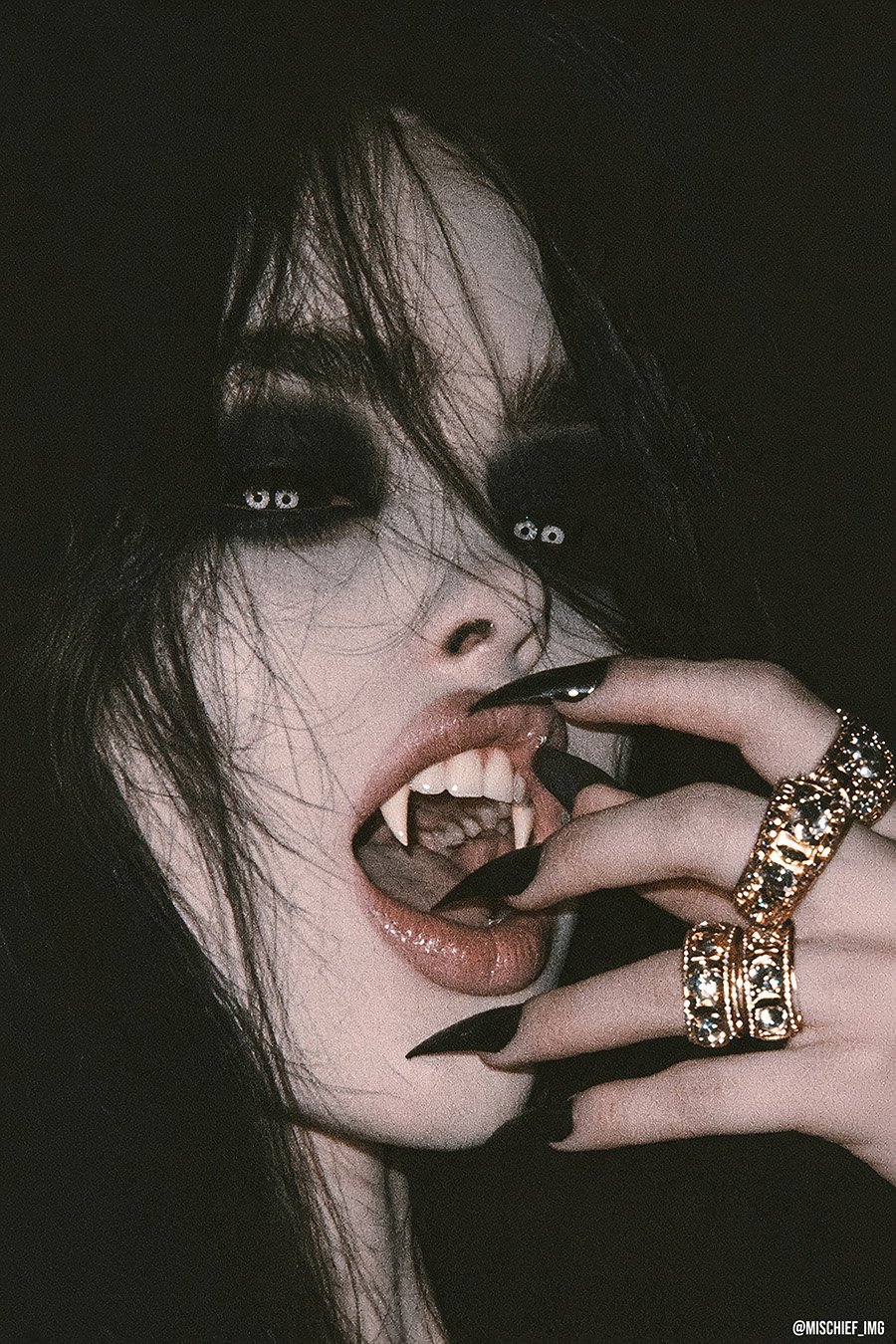 Enticing Thirst — a pale vampire with black-ringed eyes and tangled dark hair baring her fangs, a ringed finger pulling at her lip, finished in deliberate heavy antique-photo grain